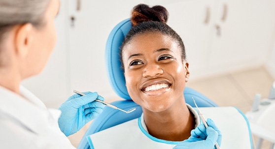 Woman in blue dental chair smiling at dentist about to examine her mouth