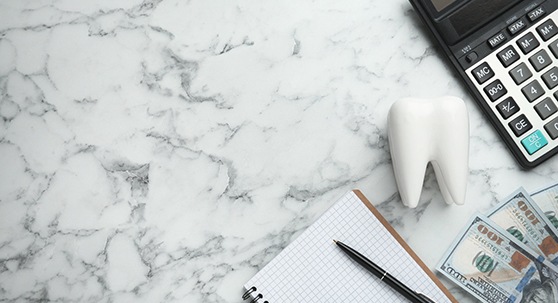 Bird’s eye view of pen, notebook, model tooth, money, and calculator on marbled surface