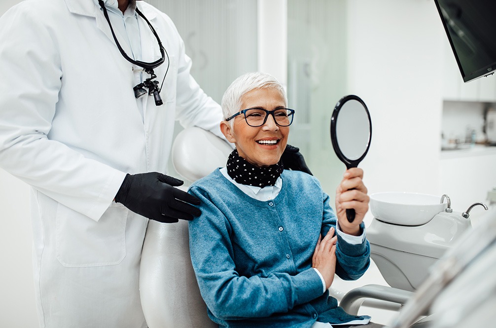 Happy senior dental patient admiring her smile in the mirror