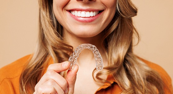 Woman in orange blouse smiling and holding Invisalign aligner